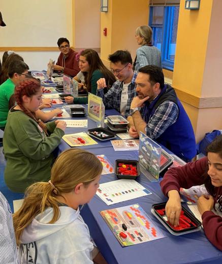 STEM fair booths with LEGO models of molecules. Adult volunteers are guiding students of all ages to build the models.